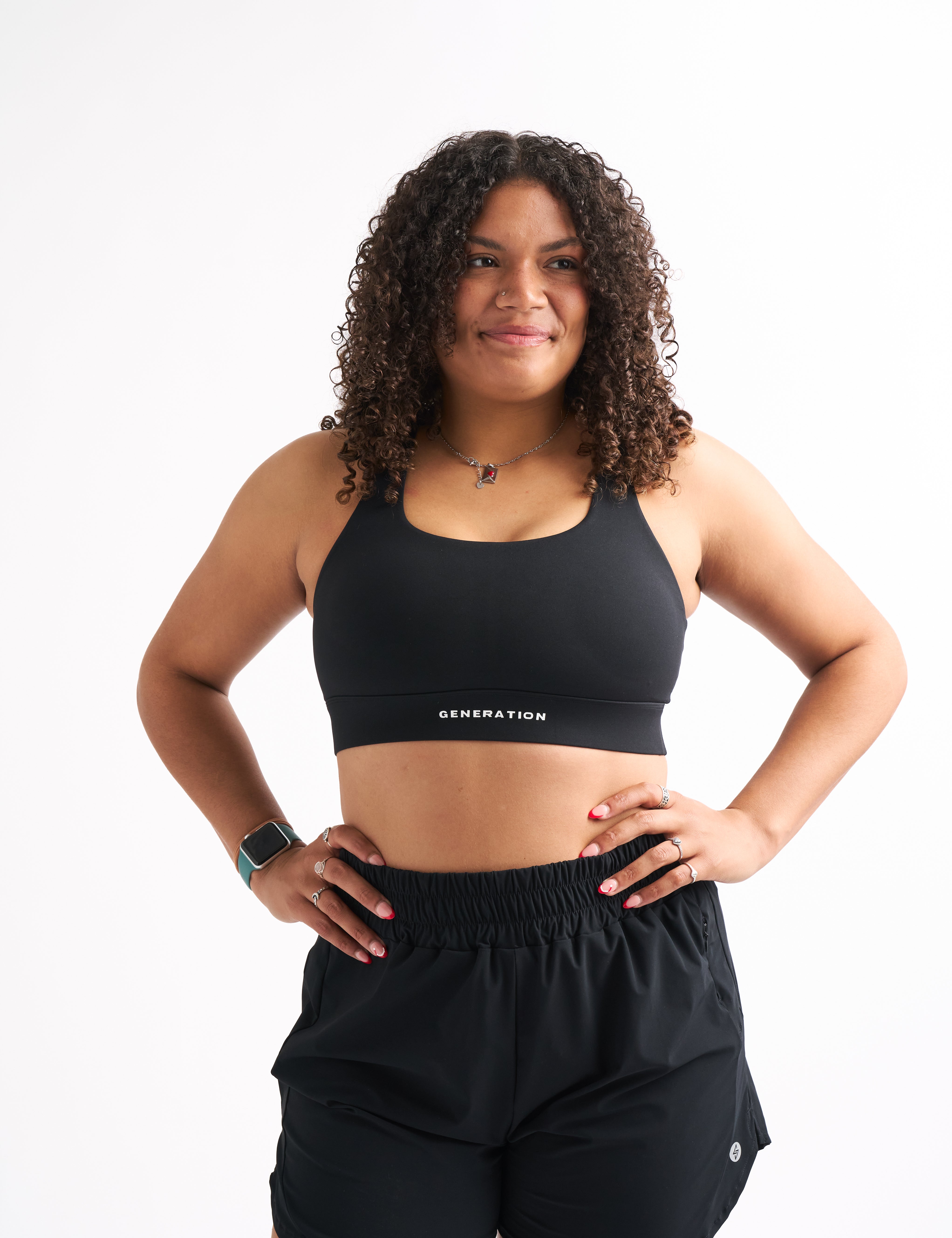 Woman facing forward in a black ZERO G sports bra with longline cut, hands on hips.