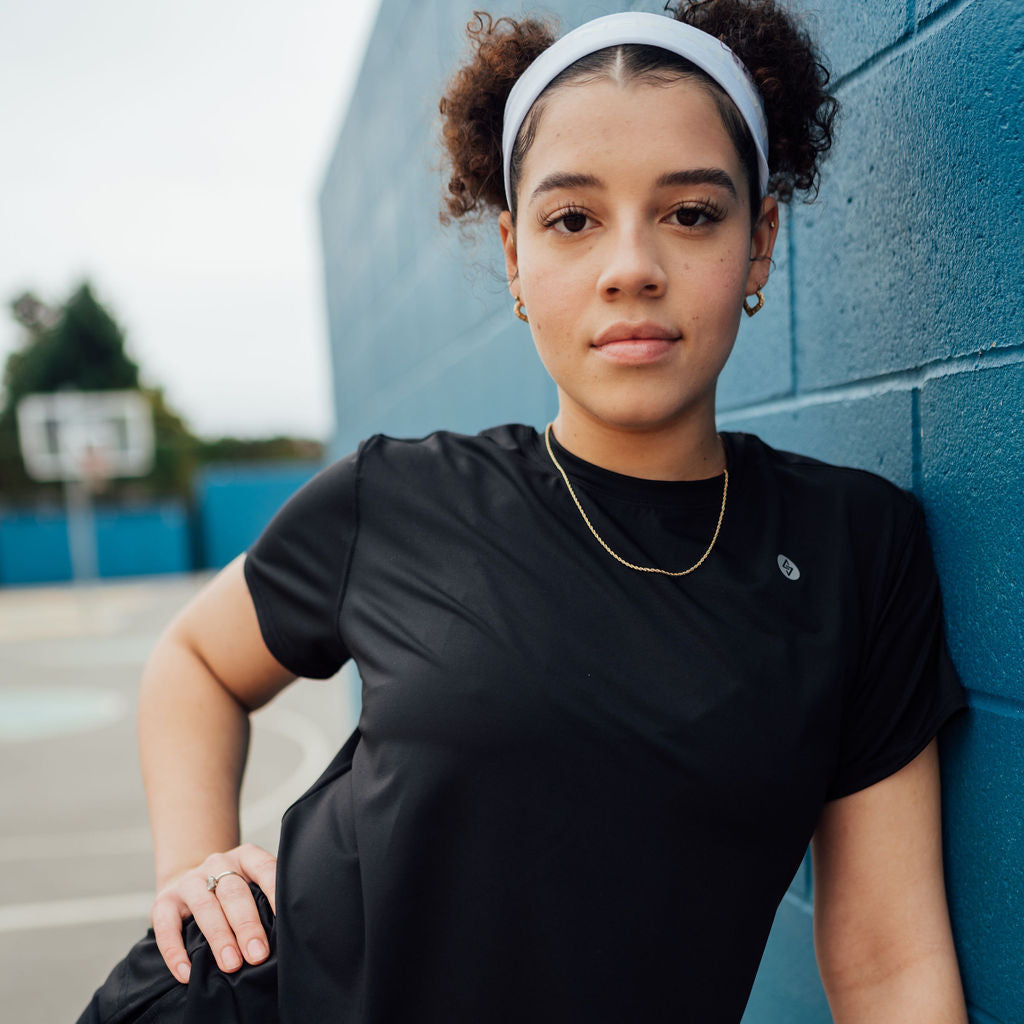 Woman in black relaxed workout shirt next to a brick wall.