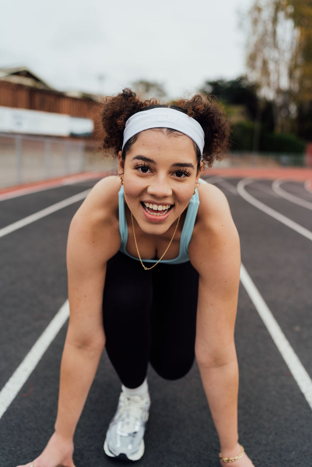 Smiling woman in a sports bra and leggings crouches on a track in a sprinter's starting position.