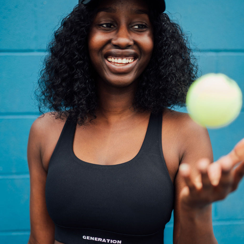 Woman in sports bra holding a tennis ball.