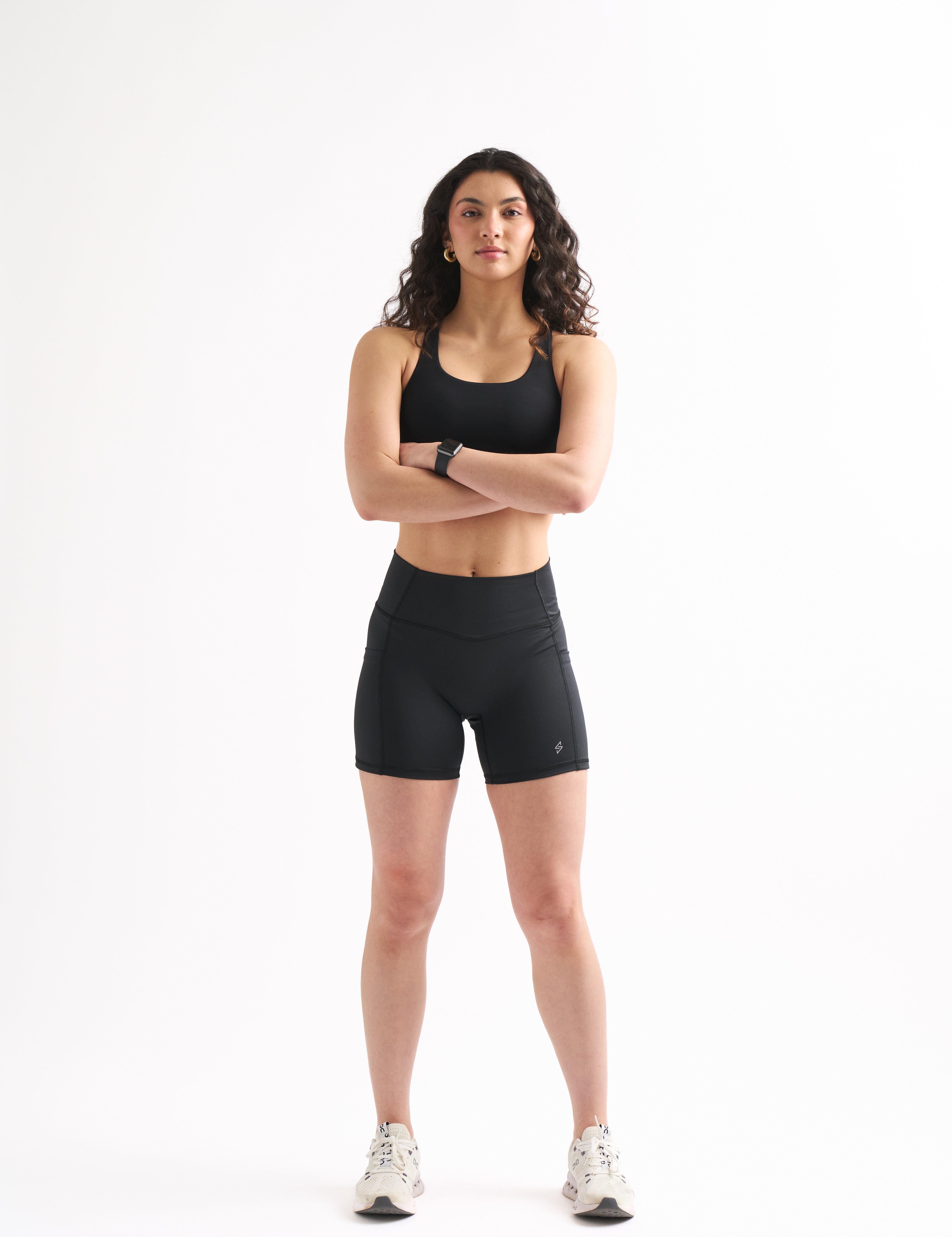 Woman wearing black Assist High Rise Shorts and a sports bra, standing confidently with arms crossed.