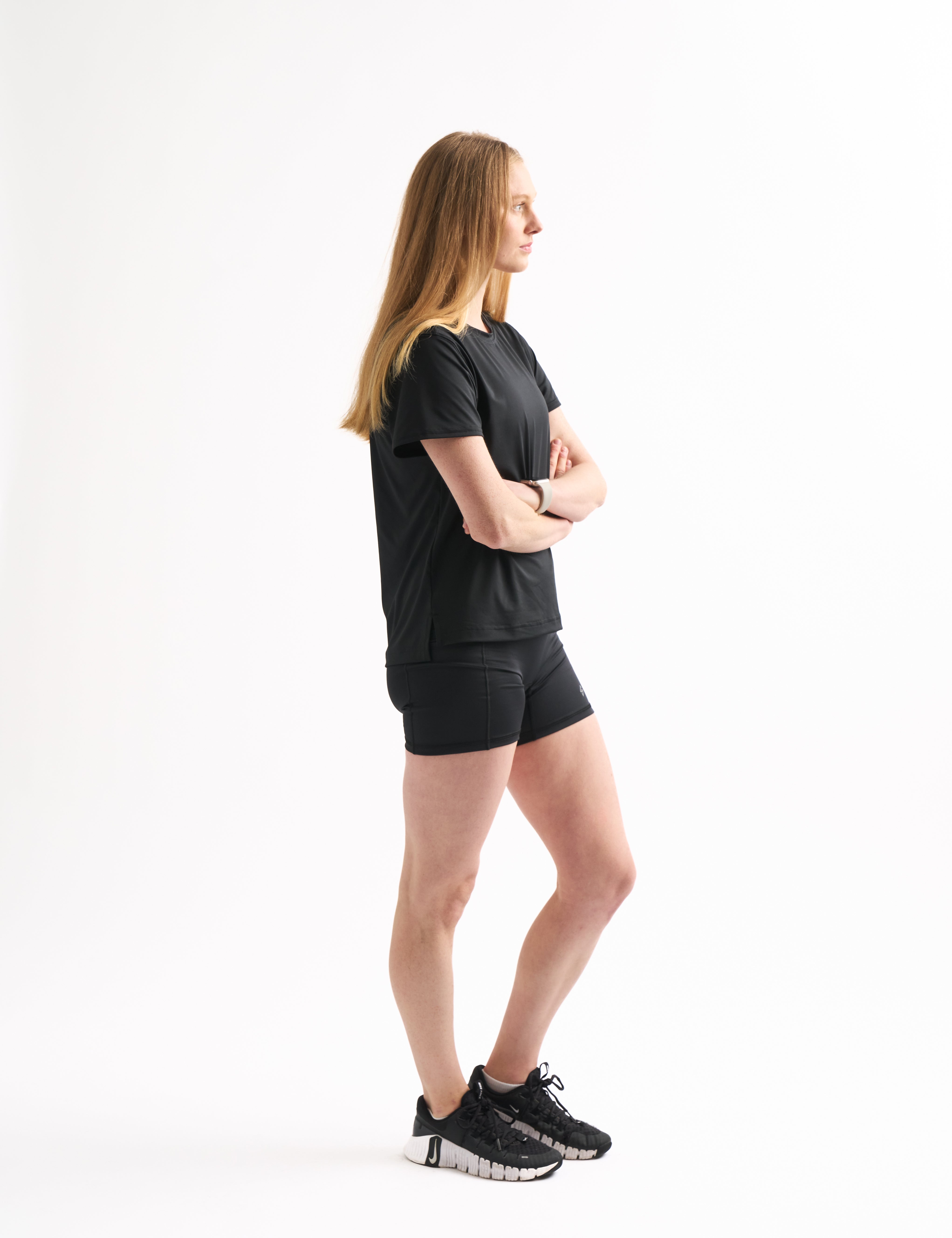 Side profile of woman in Assist High Rise Shorts with arms crossed, showing compression fit and clean seams.