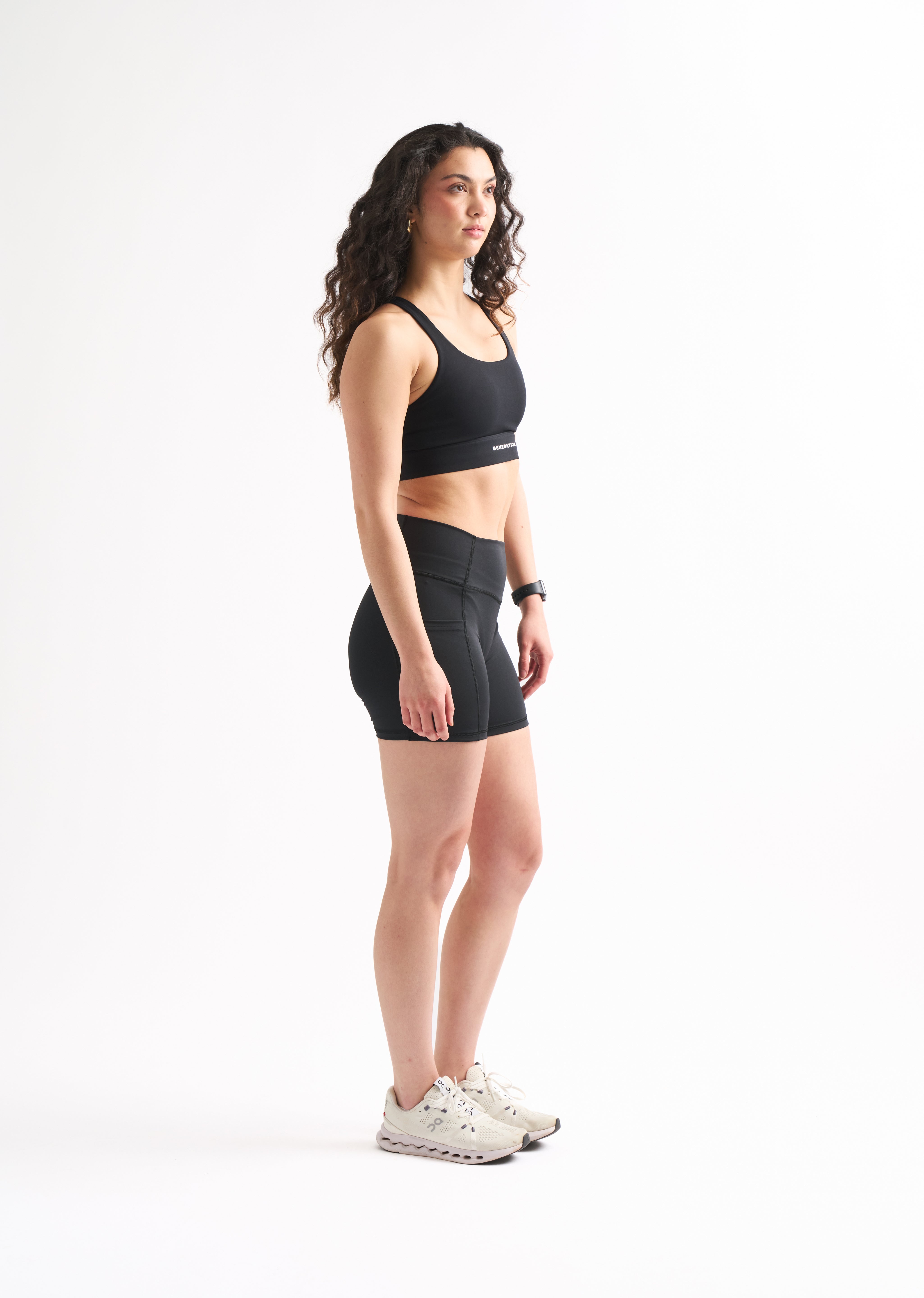 Side profile of woman in Assist High Rise Shorts with arms crossed, showing compression fit and clean seams.