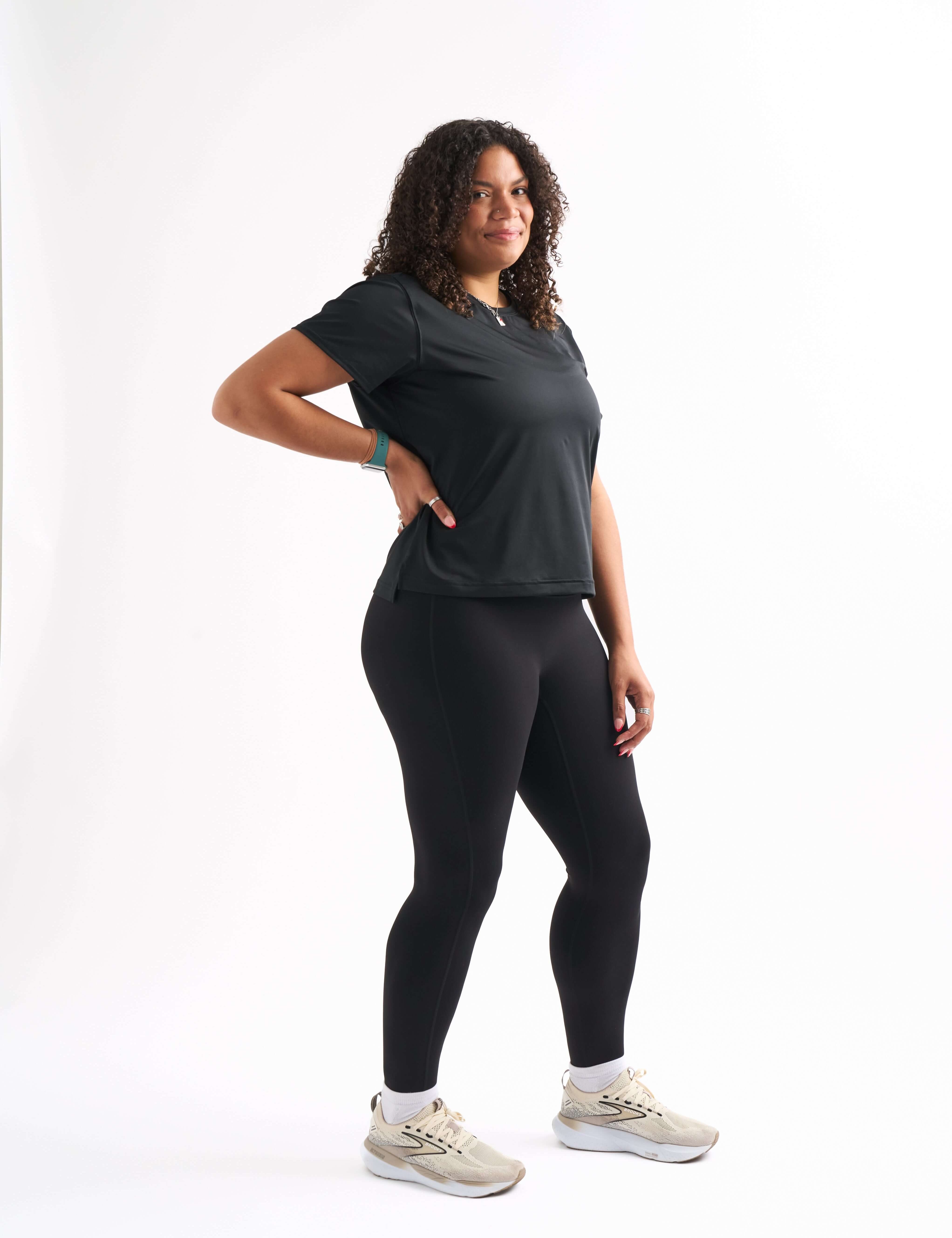 Woman standing with one leg bent and hand on her hip, wearing the Flow State top and shorts, smiling slightly.