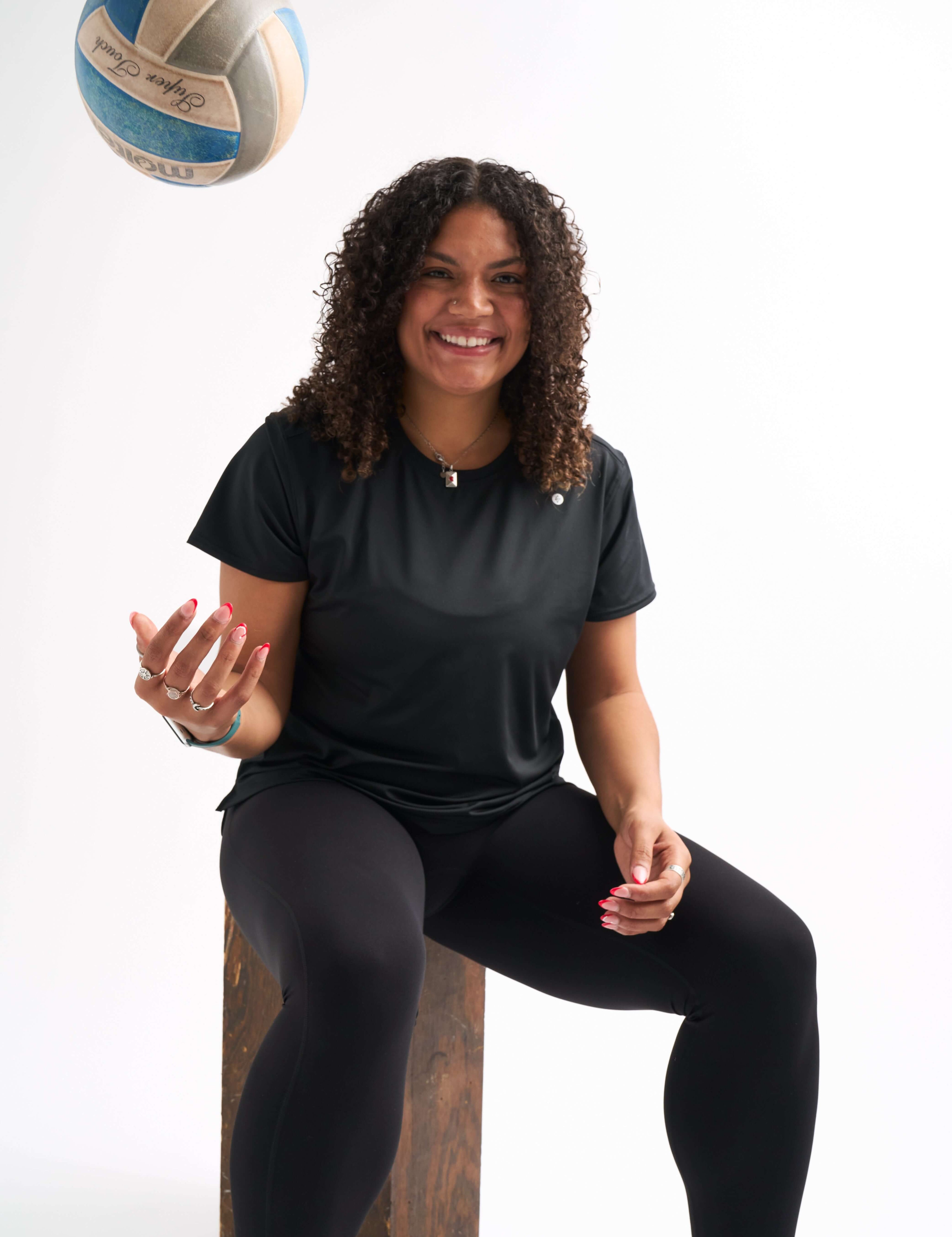 Woman wearing black Groundwork Highrise Leggings sitting on a box and tossing a volleyball mid-air.