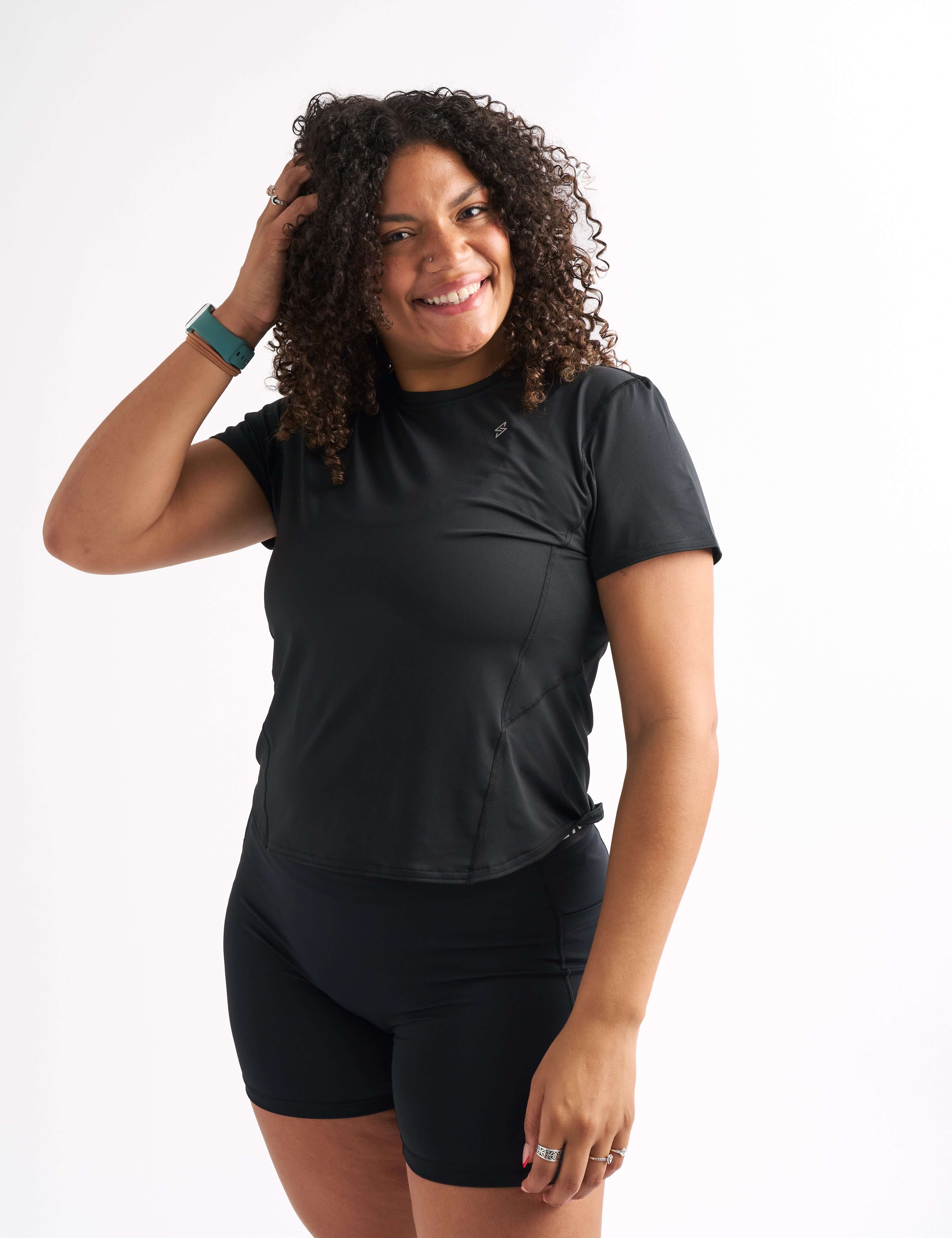 Woman wearing in fitted workout shirt, smiling with one hand in her hair.