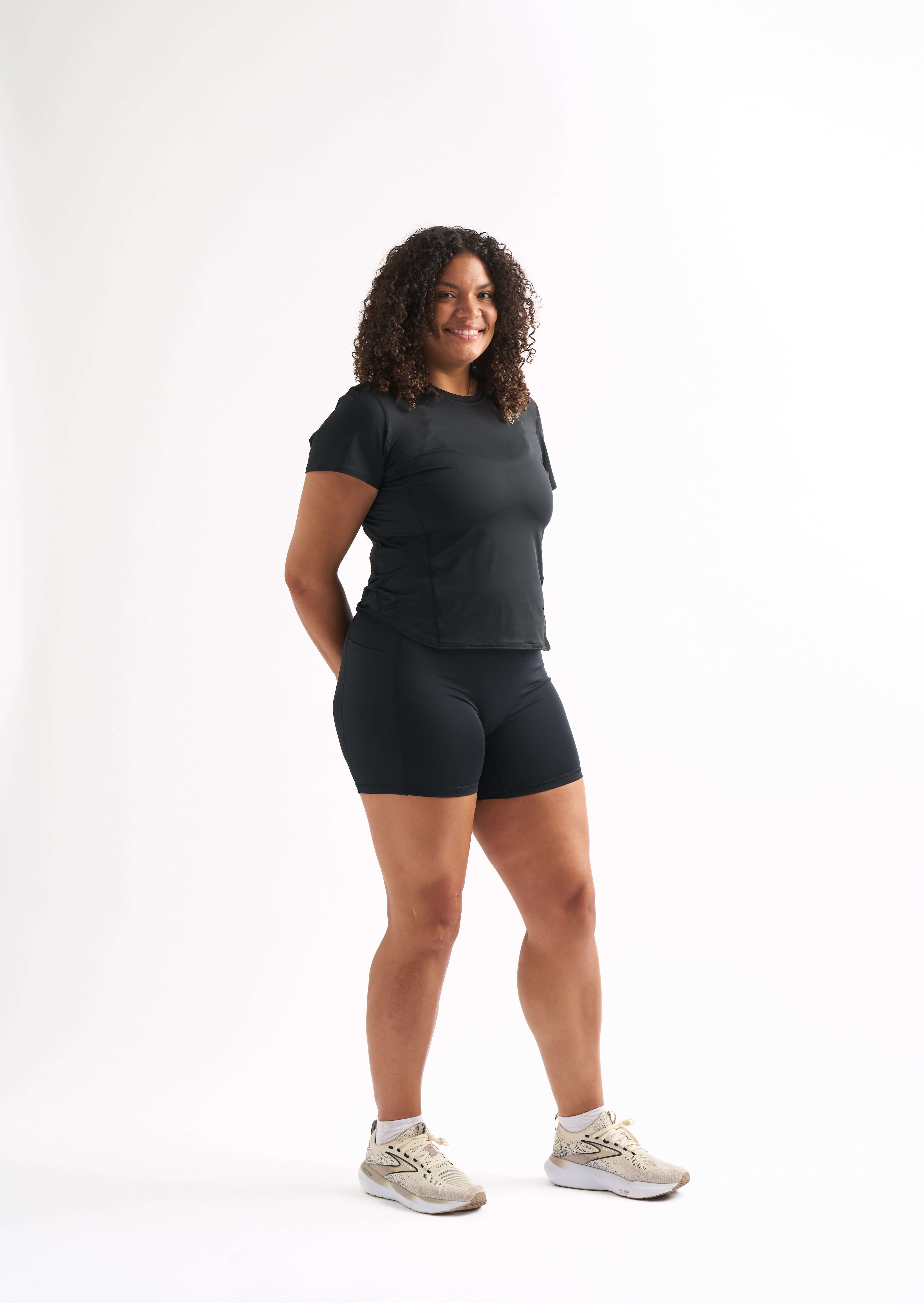 Side profile of woman wearing fitted workout shirt, smiling and hands behind her back.