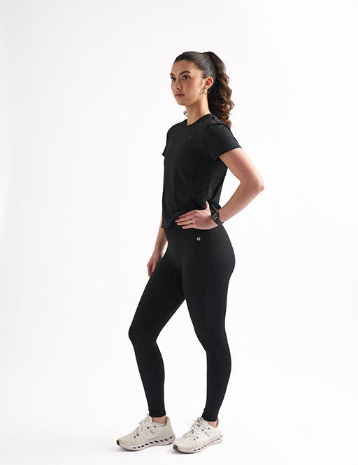 Model in fitted black workout shirt and leggings, showcasing breathability and sweat-proof performance for active women.
