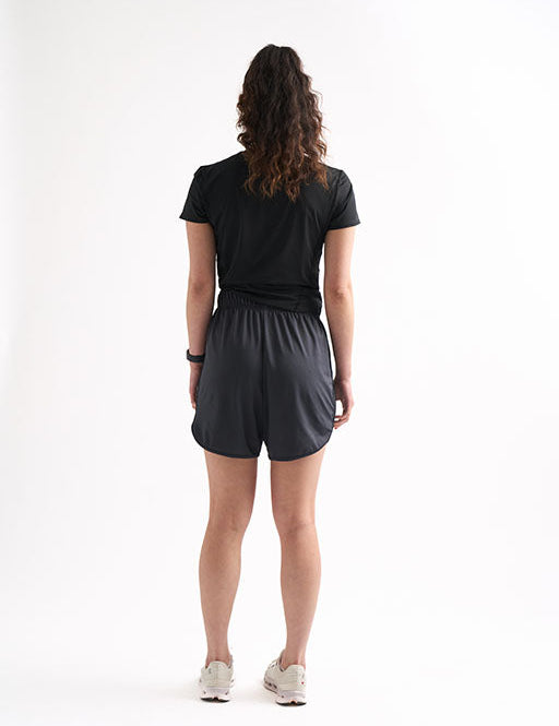 Back view of woman wearing Locked In drawstring running shorts, standing with one hand on her hip.