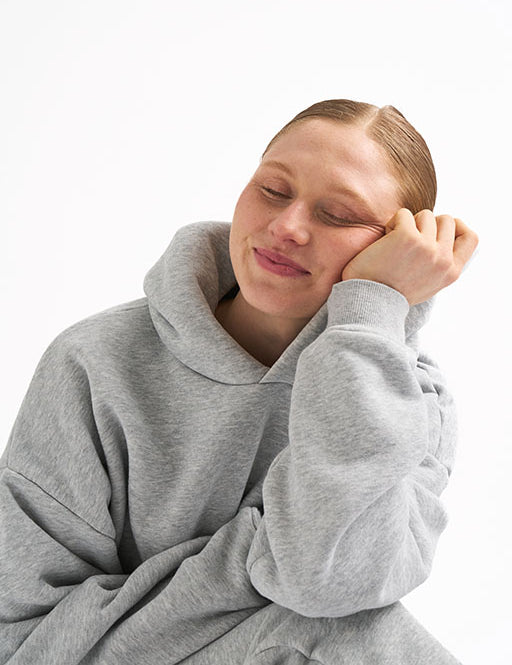 Woman wearing a light gray hoodie with classic fit, smiling with her head resting on her hand