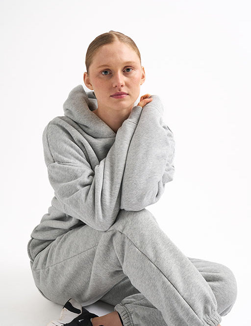 Woman sitting in light gray classic fleece-lined joggers and matching hoodie, arms wrapped around her knees