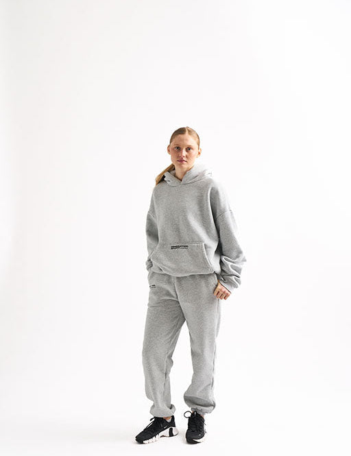 Woman wearing a light gray fleece-lined hoodie and jogger sweat set, standing facing forward with hands by her sides.