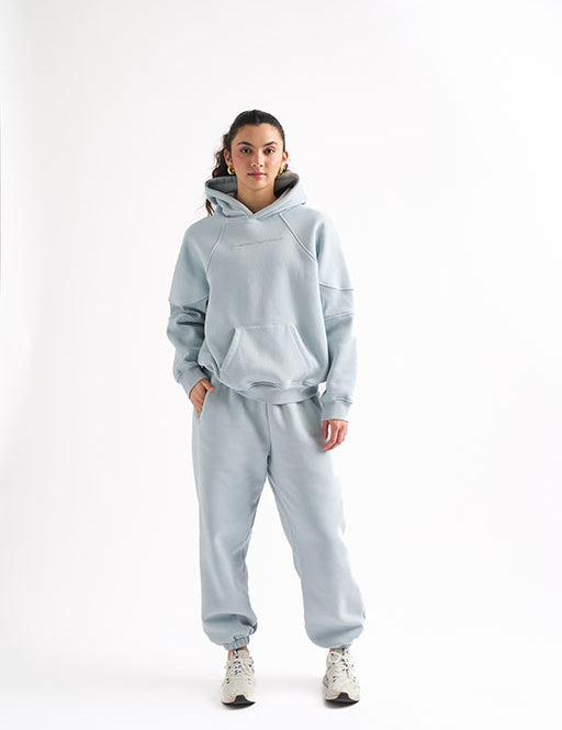 Woman wearing a light blue oversized sweat set with one hand in her hoodie pocket, standing in a confident pose.