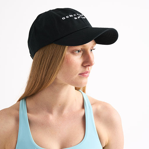 Woman wearing a black cap and sports bra, looking off to the side against a white background.