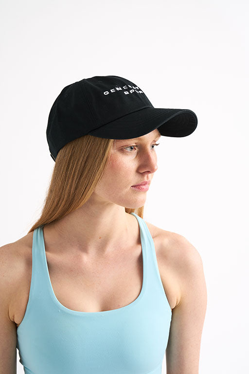 Woman wearing a black cap and sports bra, looking off to the side against a white background.