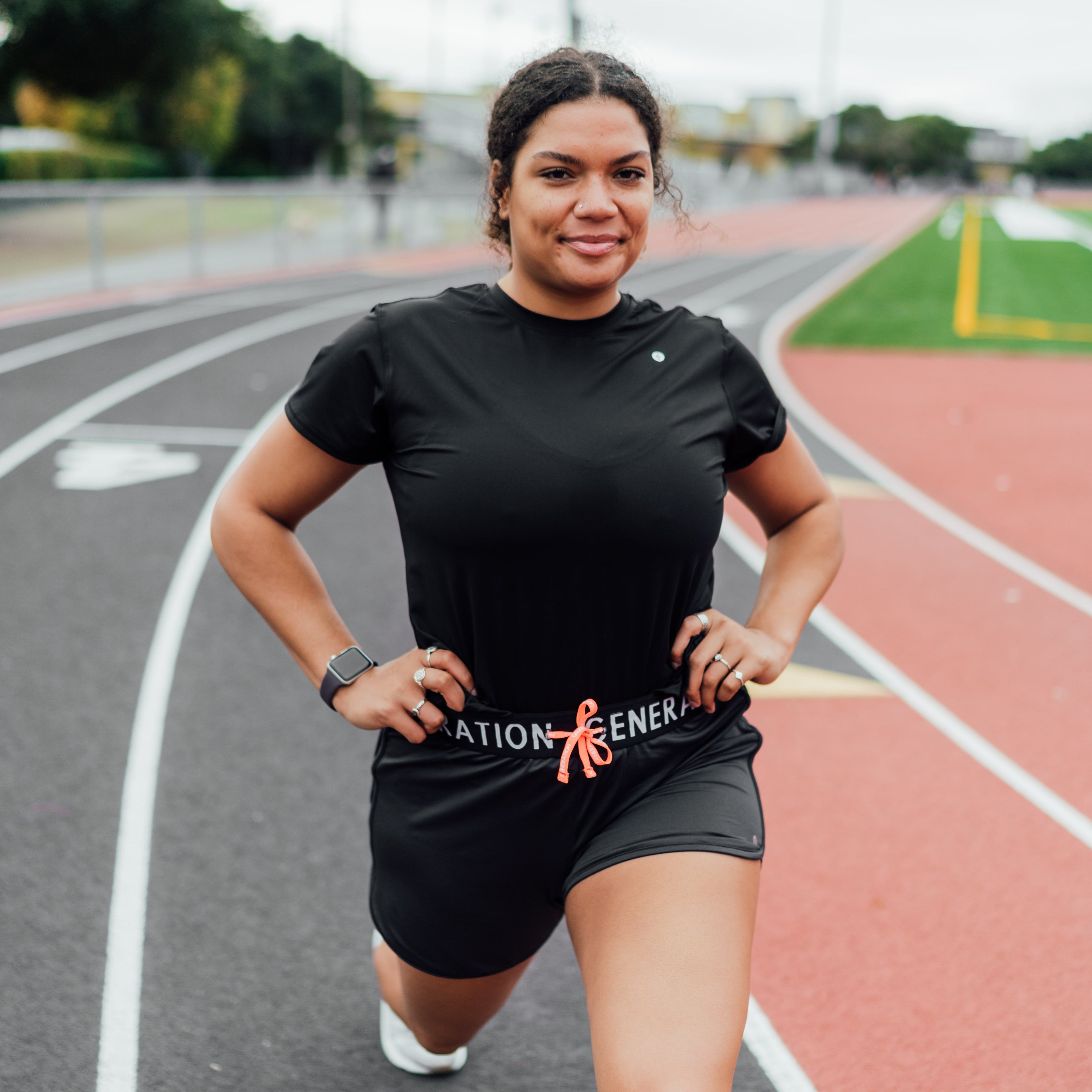 Woman stretching on a track while wearing a light blue sports bra and black shorts from Generation Sport.
