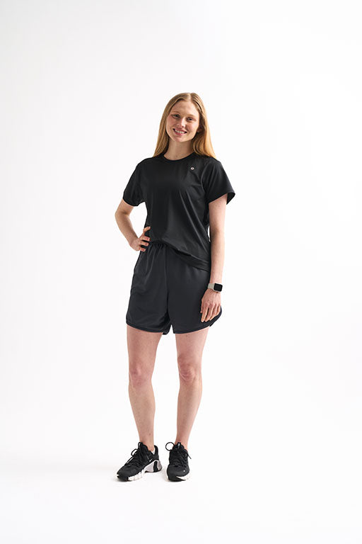 Woman wearing Locked In running shorts and a matching T-shirt, standing with one hand on her hip and smiling.