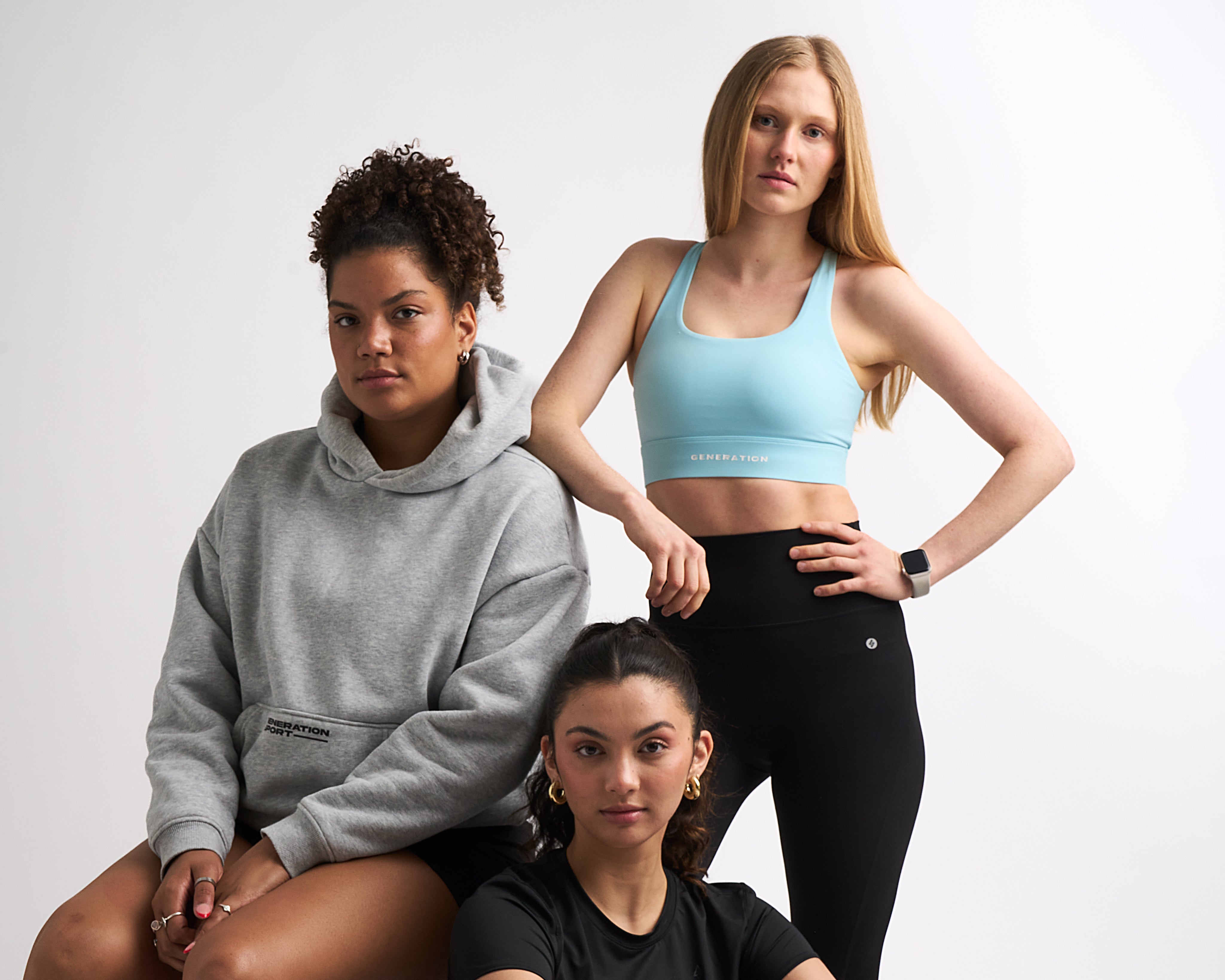 Three women in activewear: one in a hoodie, one in a sports bra and leggings, one in a black tee.