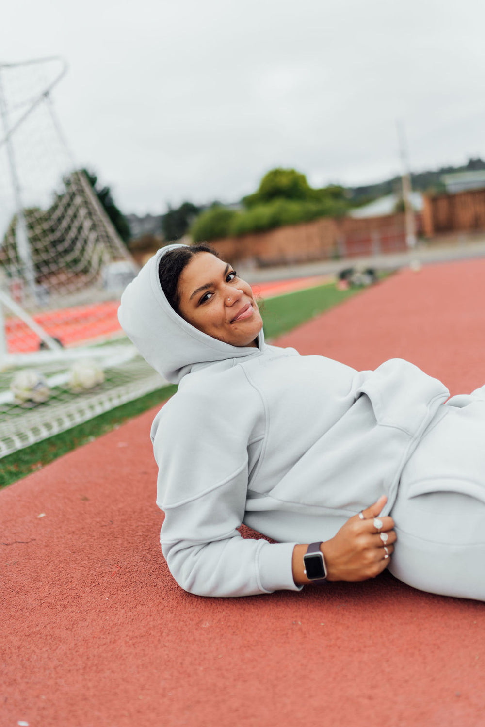 Woman wearing a light gray hoodie and pants sitting on a track field.