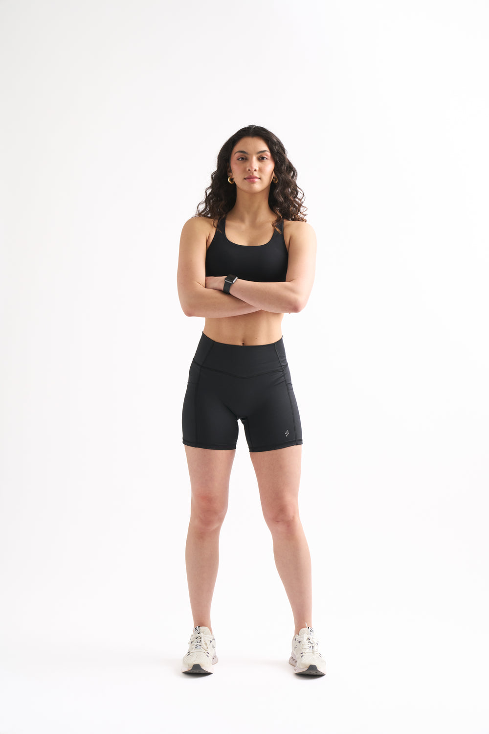 Woman wearing black Assist High Rise Shorts and a sports bra, standing confidently with arms crossed.