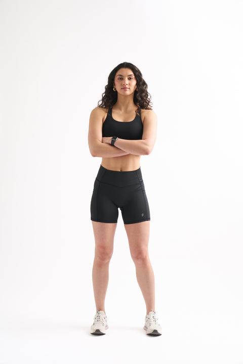 Woman wearing black Assist High Rise Shorts and a sports bra, standing confidently with arms crossed.