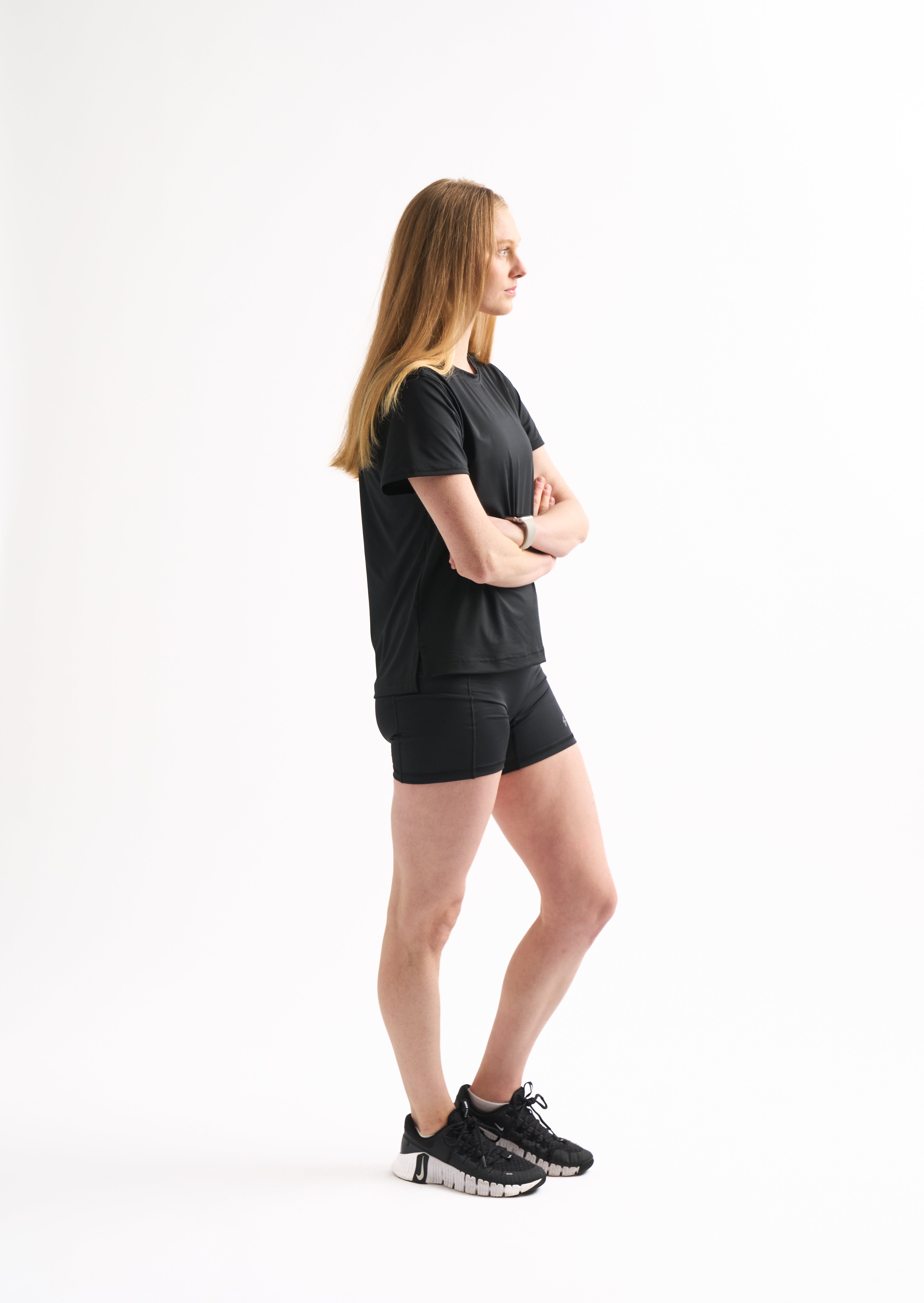 Side profile of woman in Assist High Rise Shorts with arms crossed, showing compression fit and clean seams.