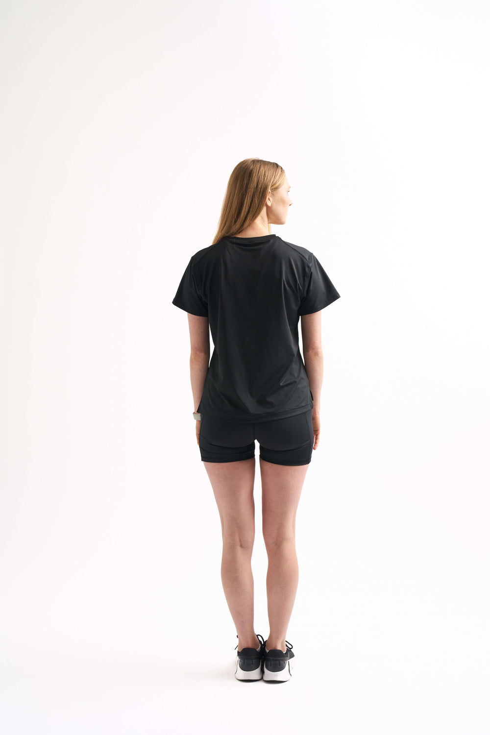 Back view of woman wearing the Flow State Relaxed Shortsleeve Top in black. Breathable training top made for movement.
