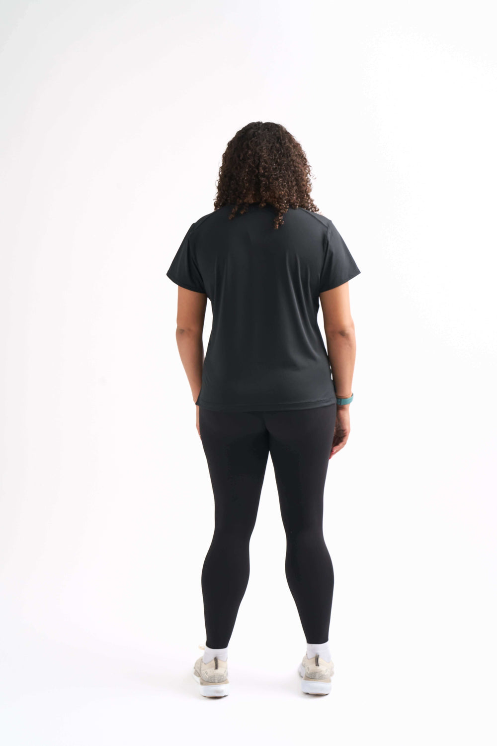 Back view of a woman wearing the Flow State top paired with black leggings, arms at sides.