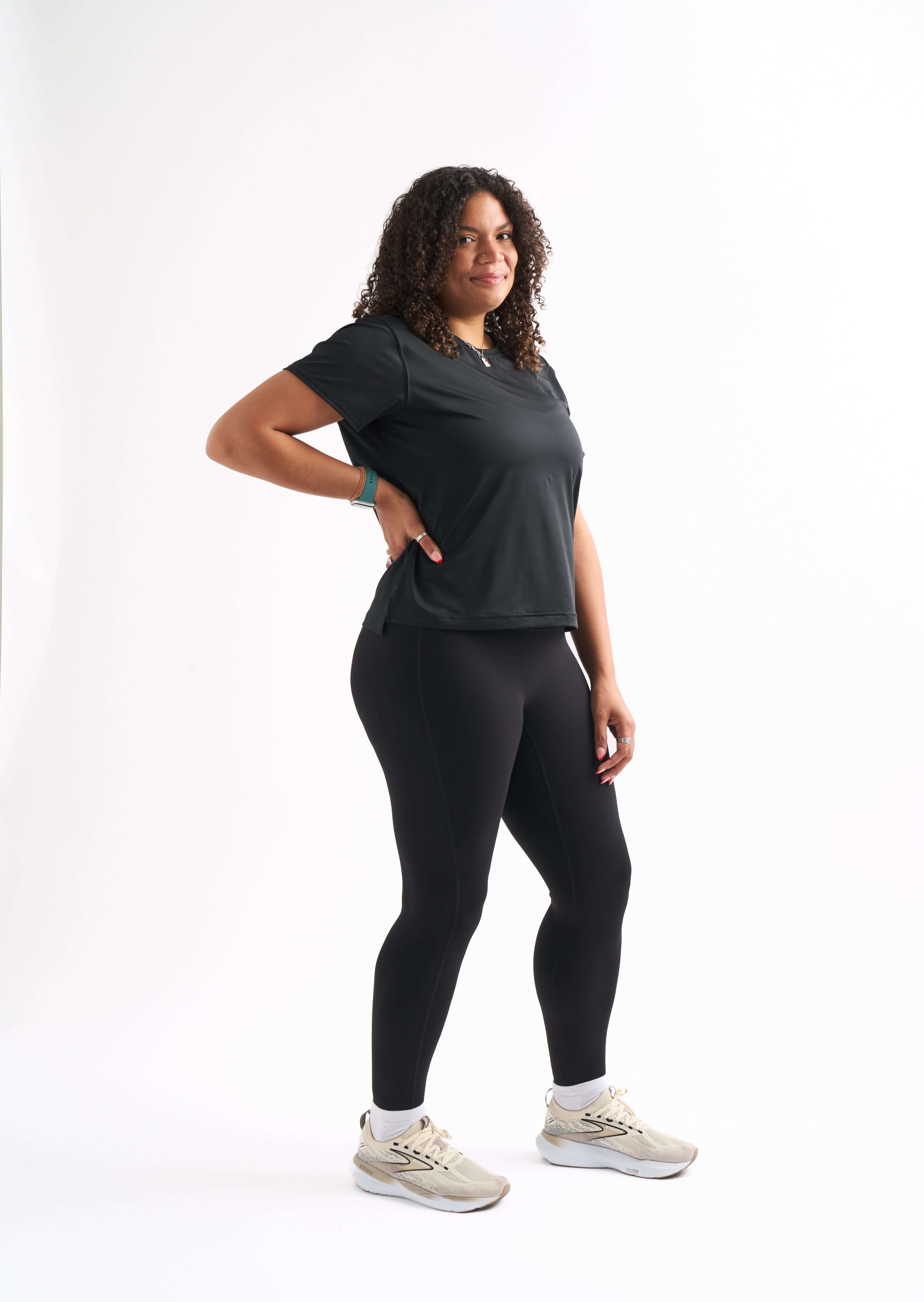 Woman standing with one leg bent and hand on her hip, wearing the Flow State top and shorts, smiling slightly.
