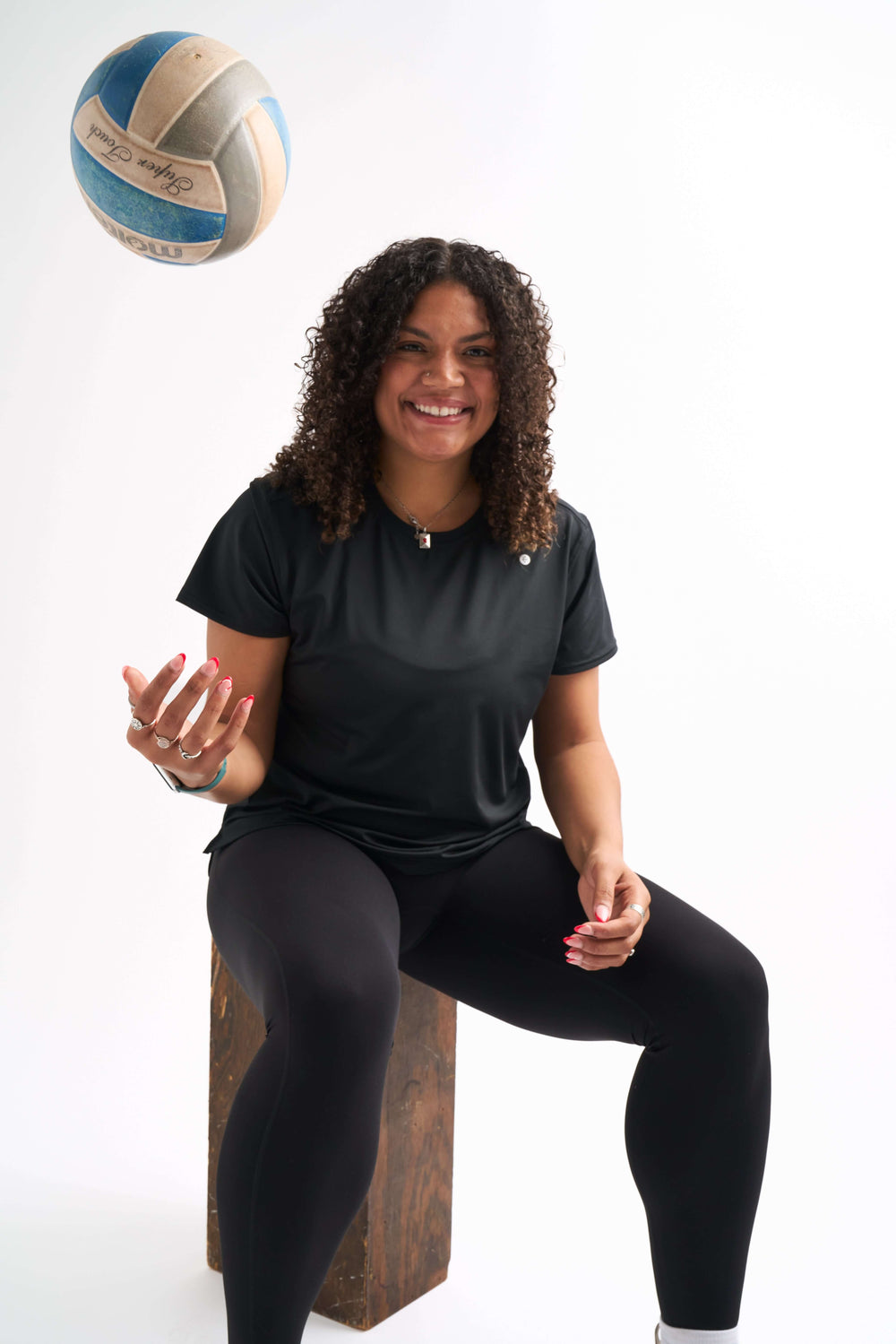 Woman wearing black Groundwork Highrise Leggings sitting on a box and tossing a volleyball mid-air.