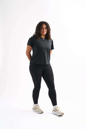 Woman wearing Groundwork High-Rise Leggings and Flow State top, standing with one leg slightly out and hands behind back.