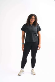 Woman standing with hands relaxed at sides, wearing Groundwork High-Rise Leggings and Flow State top with a confident smile.
