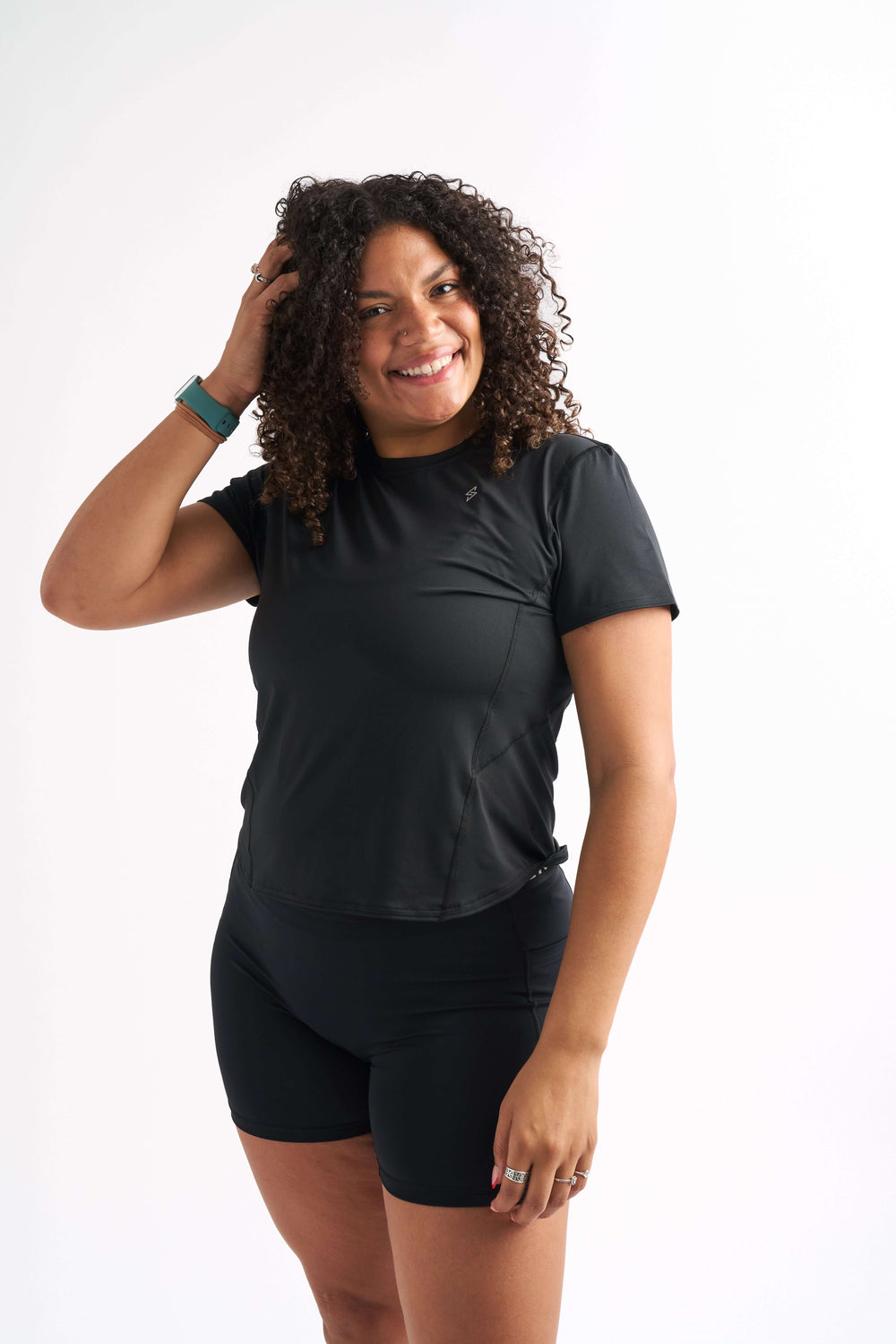 Woman wearing in fitted workout shirt, smiling with one hand in her hair.