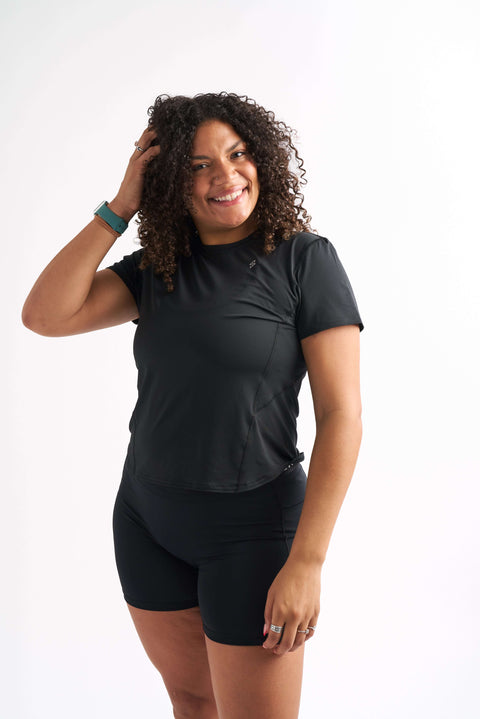Woman wearing in fitted workout shirt, smiling with one hand in her hair.