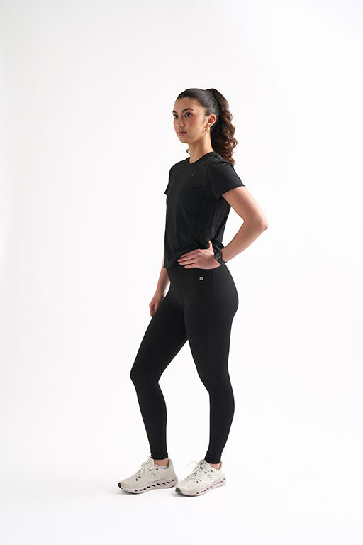 Model in fitted black workout shirt and leggings, showcasing breathability and sweat-proof performance for active women.