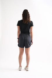 Back view of woman wearing Locked In drawstring running shorts, standing with one hand on her hip.