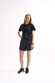 Woman wearing Locked In running shorts and a matching T-shirt, standing with one hand on her hip and smiling.
