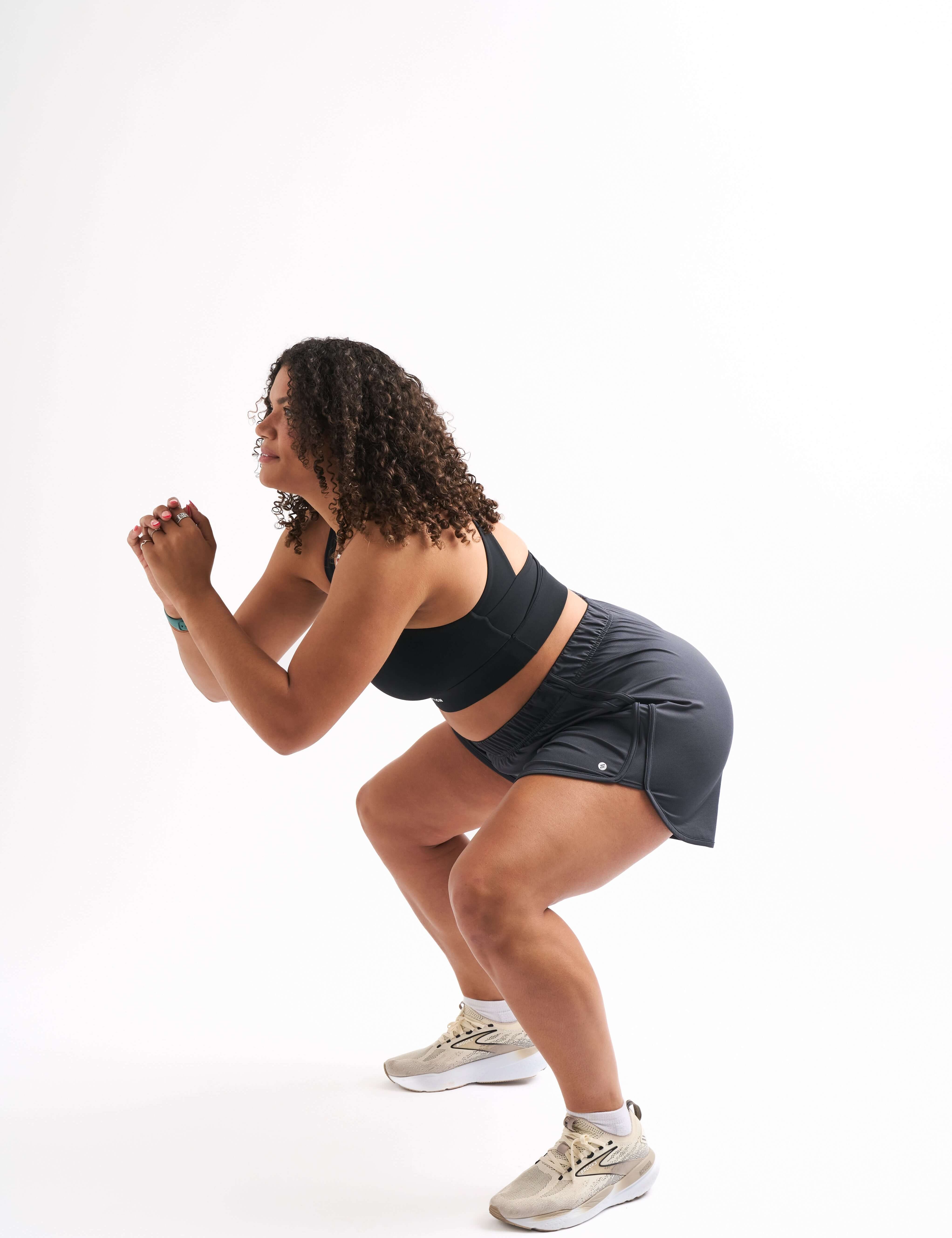 Woman squatting in breathable running shorts, showcasing style and comfort during workouts.