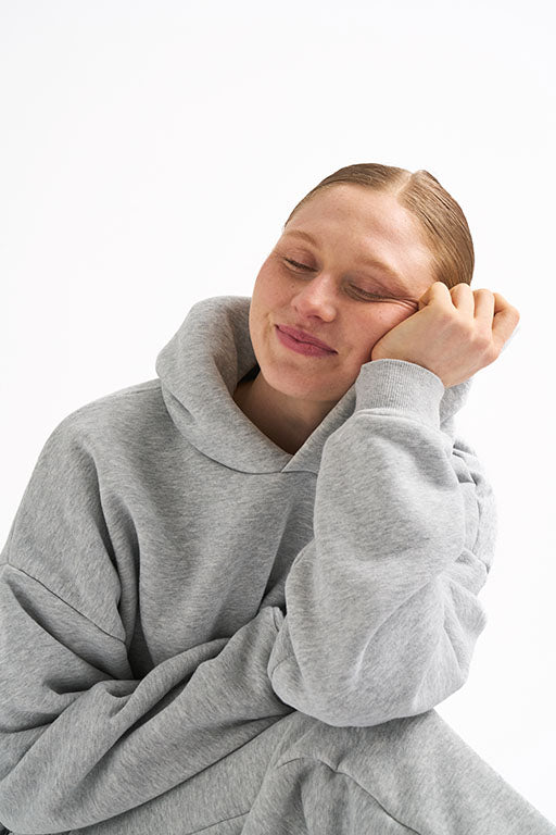 Woman wearing a light gray hoodie with classic fit, smiling with her head resting on her hand