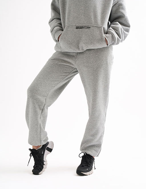 Cropped view of woman standing in light gray classic joggers with black sneakers and a Generation Sport hoodie