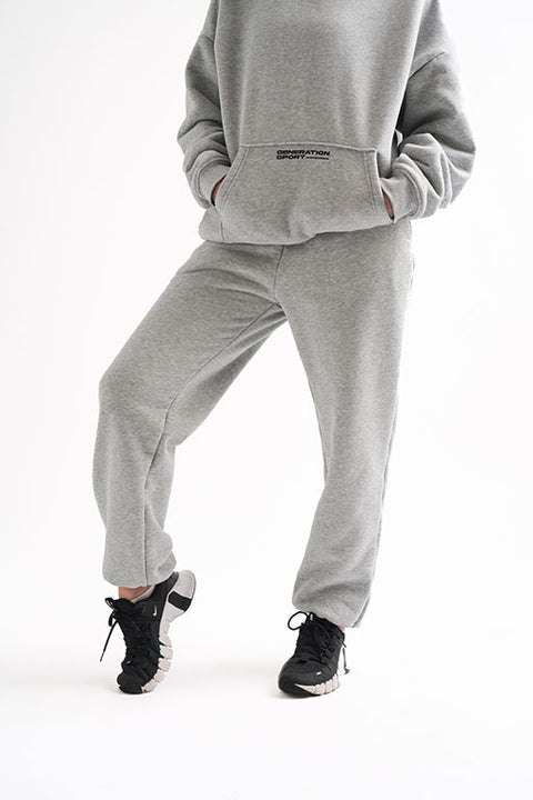 Cropped view of woman standing in light gray classic joggers with black sneakers and a Generation Sport hoodie