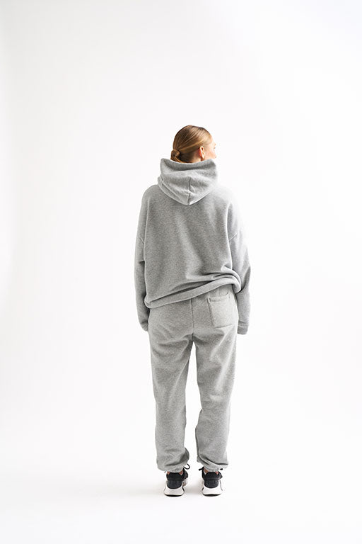 Back view of woman wearing light gray fleece hoodie and joggers and hands relaxed at sides.