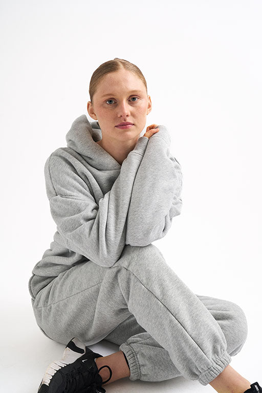 Woman sitting in light gray classic fleece-lined joggers and matching hoodie, arms wrapped around her knees