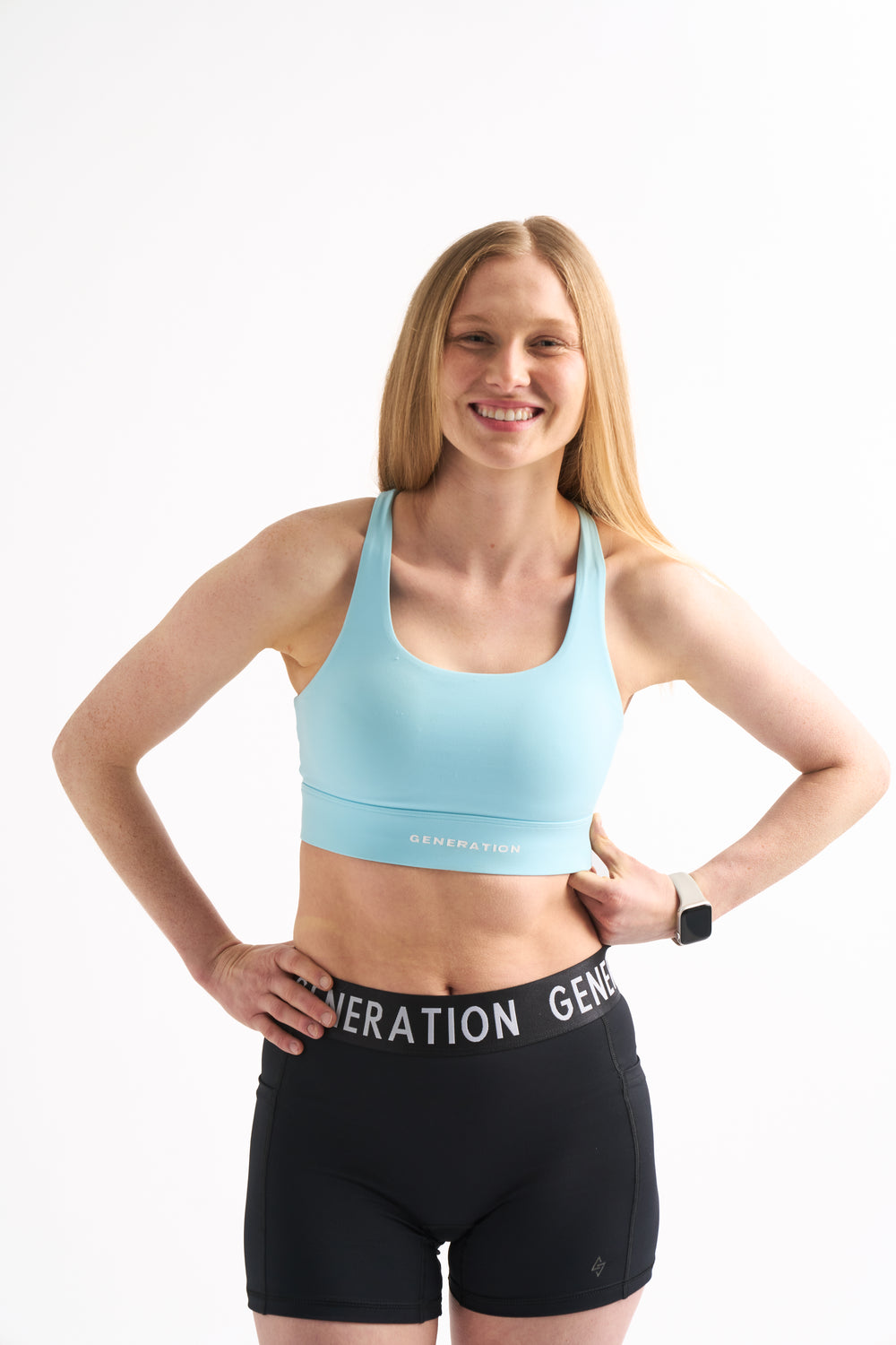 Woman wearing Power Moves Midrise Shorts and a blue Zero G sports bra, smiling with hands on hips.