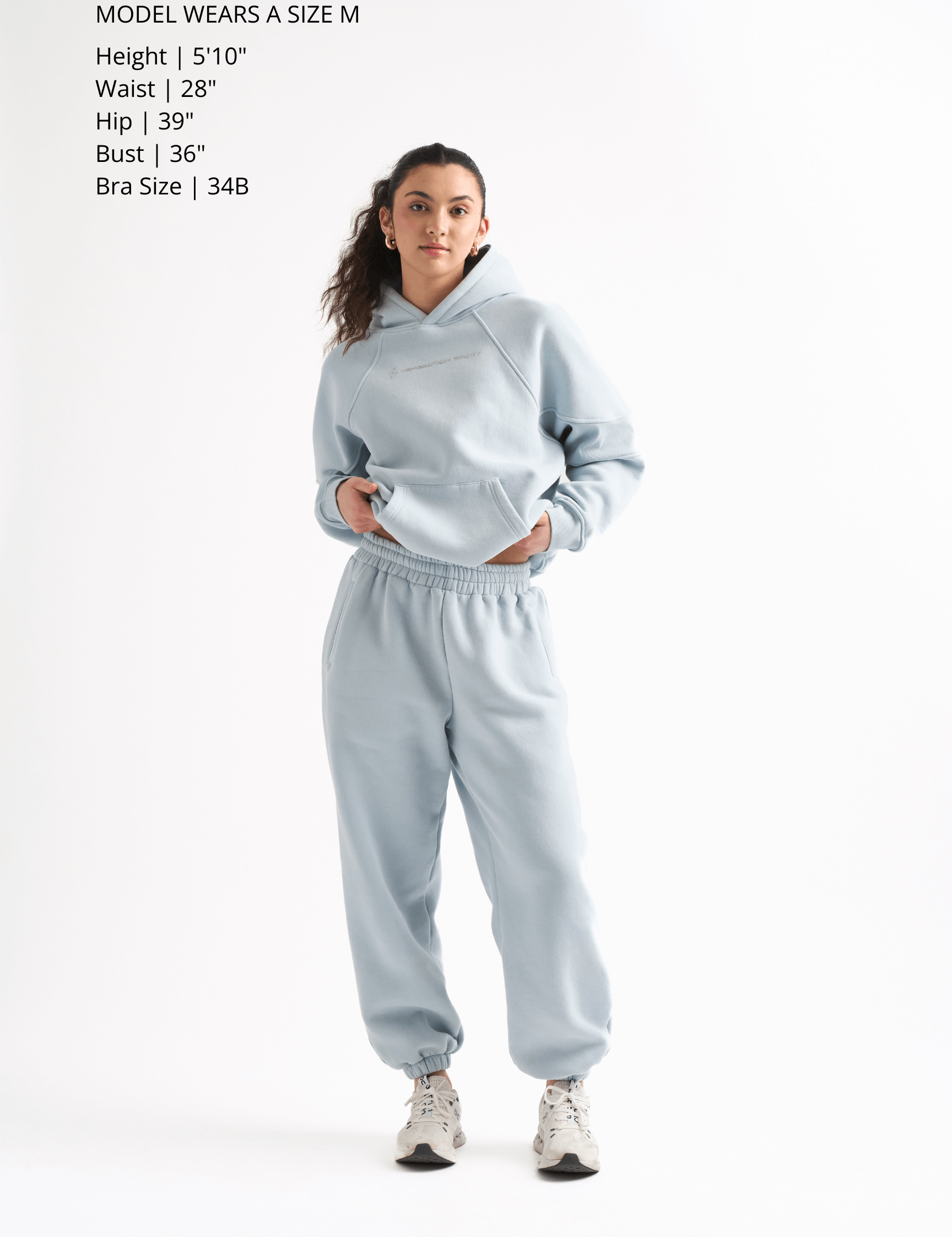 Woman wearing a light gray hoodie and sweatpants on a white background