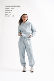 Woman wearing a light gray hoodie and sweatpants on a white background