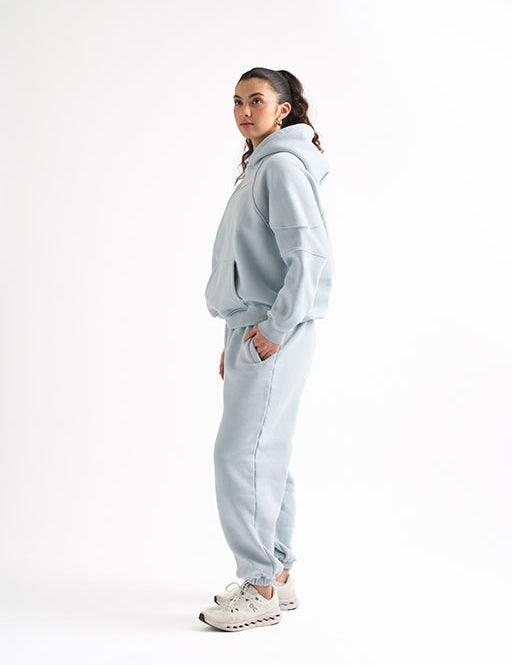 Side view of woman wearing a light blue oversized sweat set, standing with one hand in her pocket and looking ahead